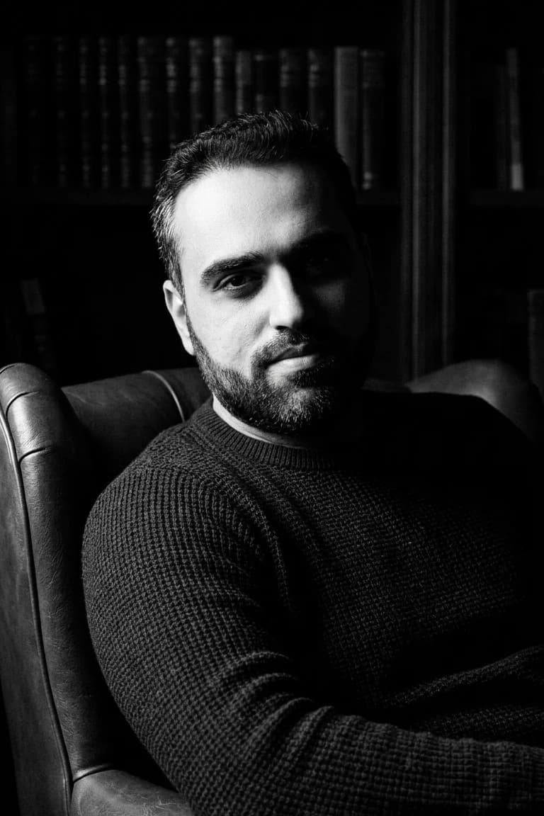 Mohammad Issam, founder of Mojawhara, seated in a leather armchair before a wall of books, photographed in black and white.