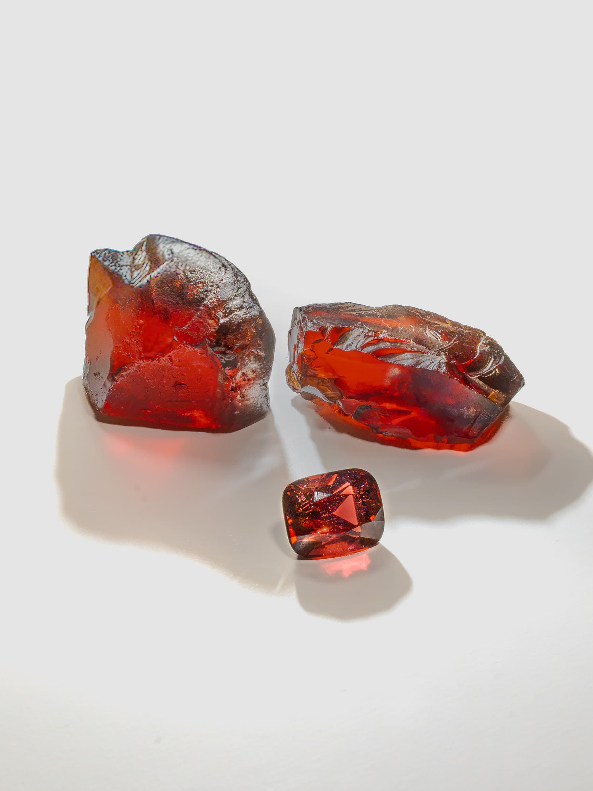 Two pieces of natural rough gemstone beside a specially cut stone.